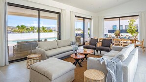 Ein geräumiges Wohnzimmer mit einer Couch, Sesseln, einem Couchtisch und Blick auf einen Pool sowie die Stadtlandschaft.