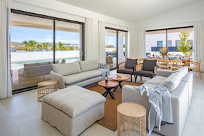 Ein geräumiges Wohnzimmer mit einer Couch, Sesseln, einem Couchtisch und Blick auf einen Pool sowie die Stadtlandschaft.