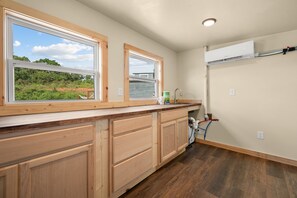 A kitchen with wooden cabinets, a built-in window, and a view of greenery outside. - Tiny Home Village Near Dollywood | Sleeps 60+ (Sevierville)