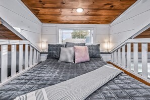 A bedroom with a bed, pillows, a bedside lamp, and a window. - Tiny Home Village Near Dollywood | Sleeps 60+ (Sevierville)