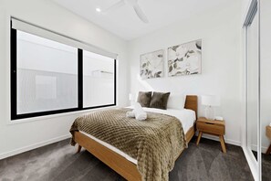Ein modernes Hotelzimmer mit großem Fenster, einem Bett mit brauner Decke, zwei Wandbildern und einem Nachttisch mit Lampe.