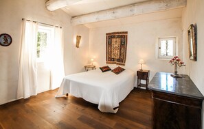 Ein Schlafzimmer mit einem großen Bett, zwei Nachttischen, einer Kommode, einem Fenster mit Vorhängen, einer Wandteppich und einem gerahmten Bild.