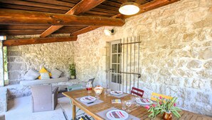 A rustic stone wall, wooden ceiling beams, a dining table set with plates and glasses, and a bench with cushions. - Awesome home in Labeaume with WiFi (Labeaume)