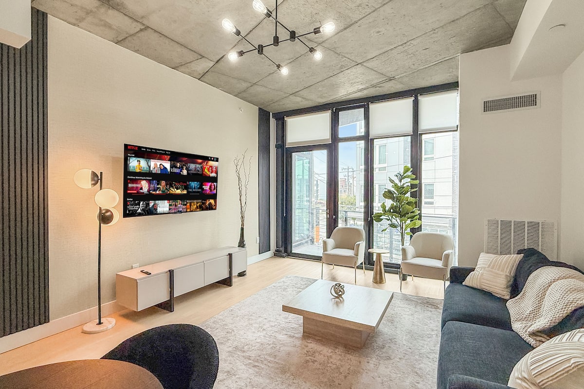 A modern living room with a flat-screen TV, a coffee table, sofas, and a large window with a city view.