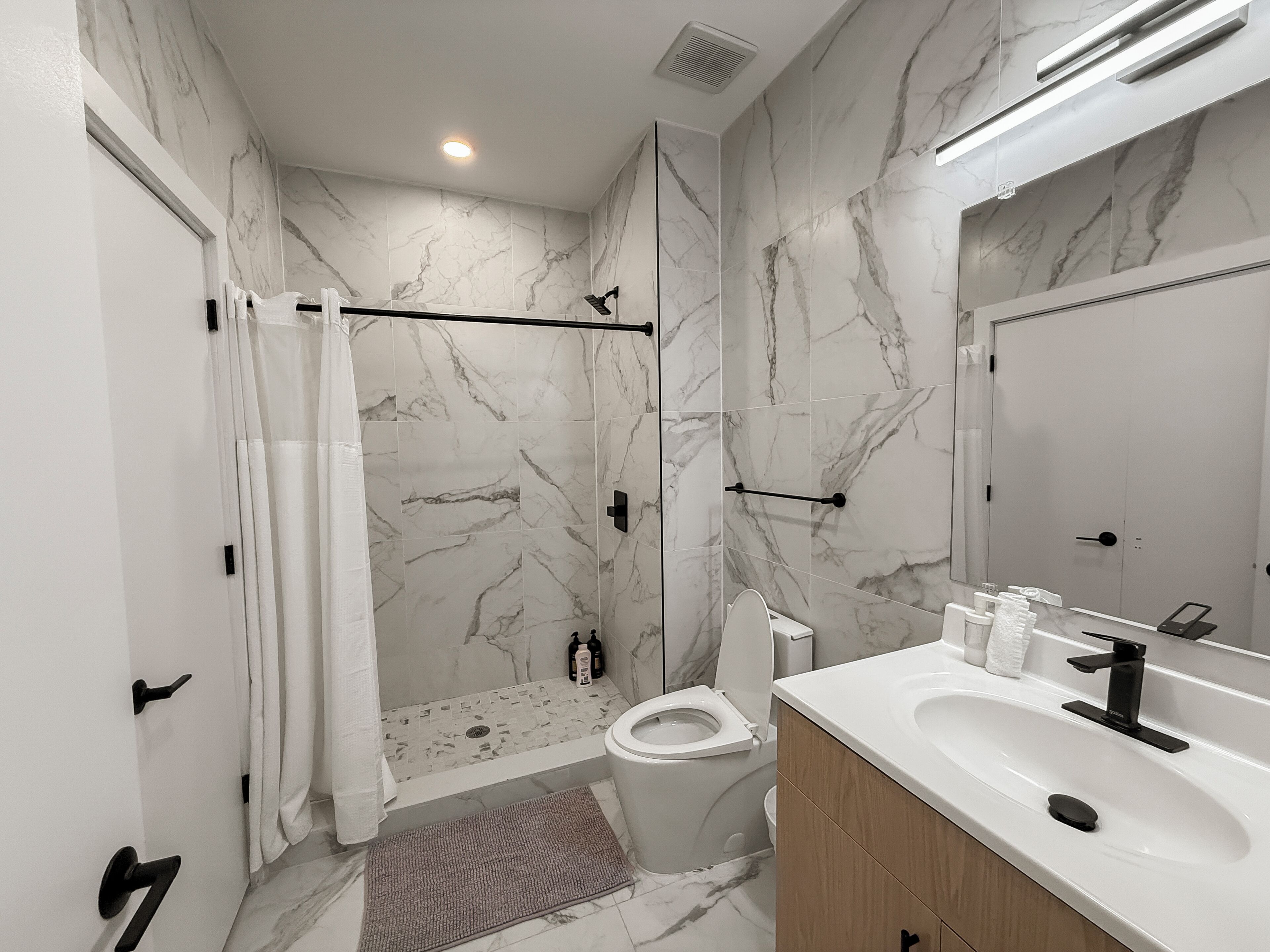 A bathroom with a shower, toilet, and sink, marble walls, and a large mirror.
