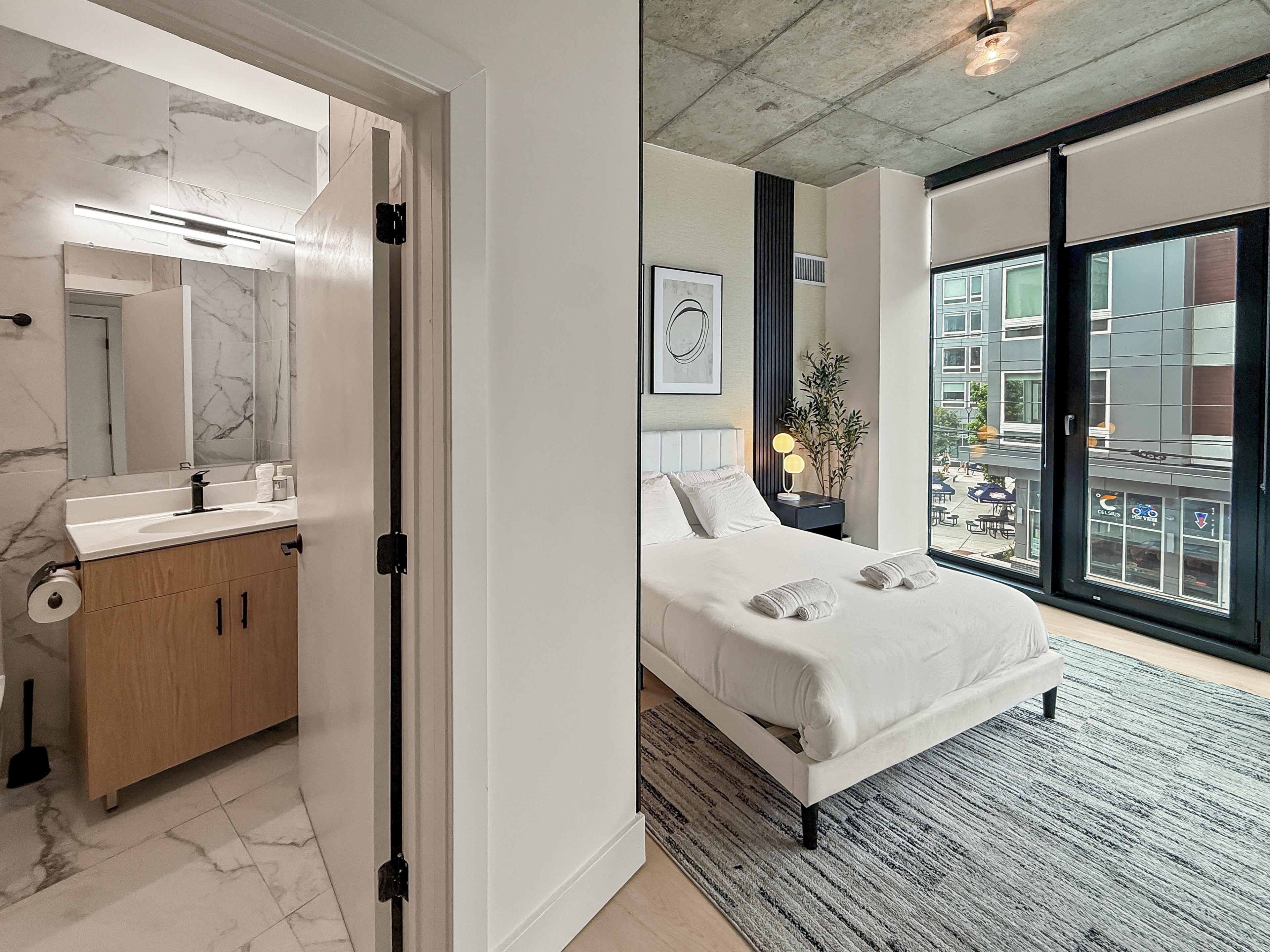 Et moderne hotelværelse med badeværelse, en stor seng, udsigt over byen og en balkon.