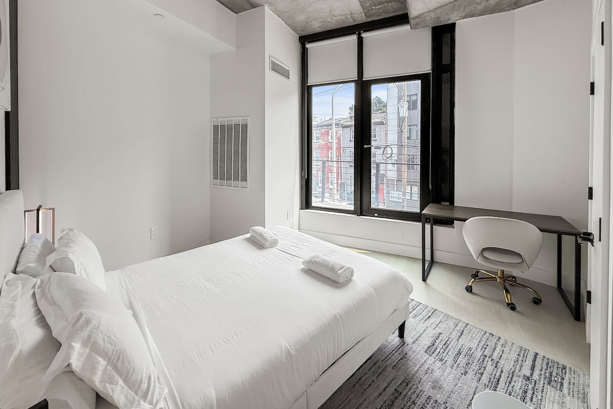 A modern hotel room with a large bed, a desk, and a view of the city.