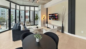 A modern living room with a large window, a sofa, a coffee table, and a TV mounted on the wall. - Apartmint at N 2nd St Philadelphia (Philadelphia)