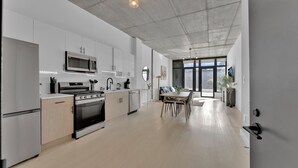 A modern kitchen with stainless steel appliances, a dining area with a wooden table and chairs, and large windows offering a view of the outside. - Apartmint at N 2nd St Philadelphia (Philadelphia)