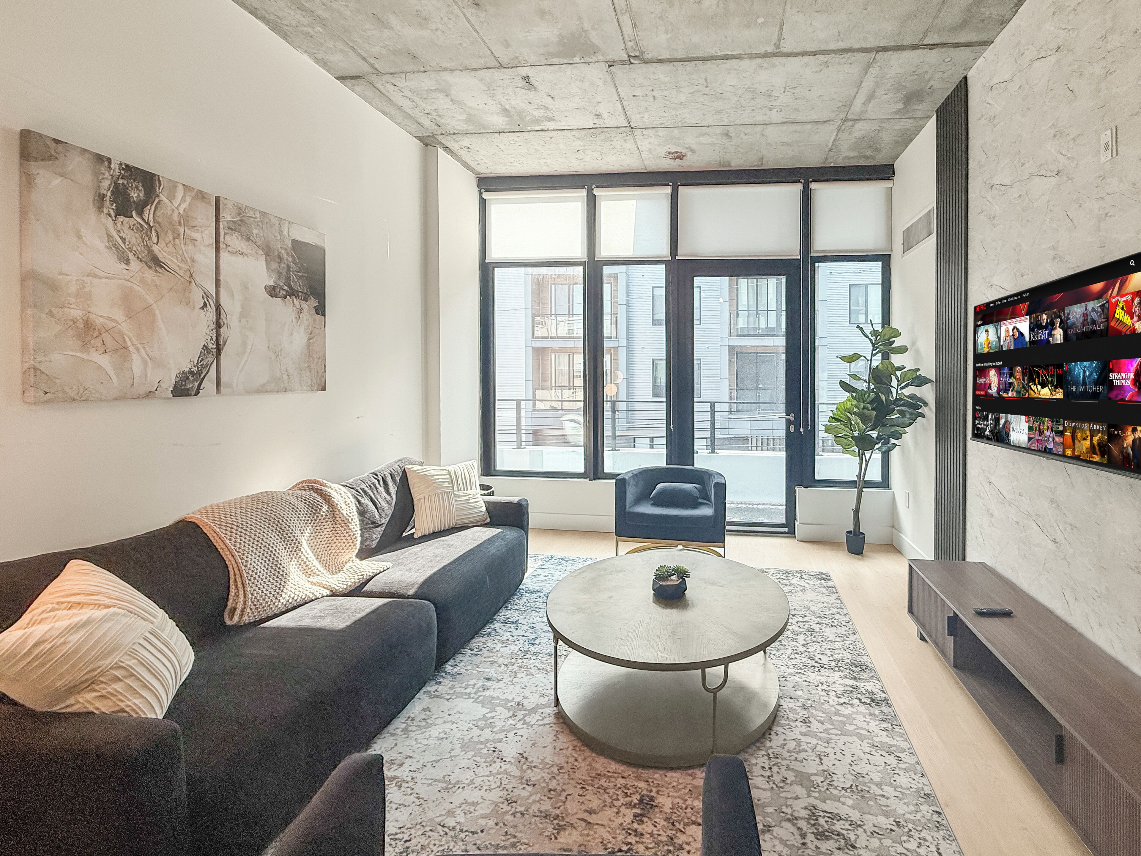 Een moderne woonkamer met een bank, salontafel, tv-meubel en grote ramen.