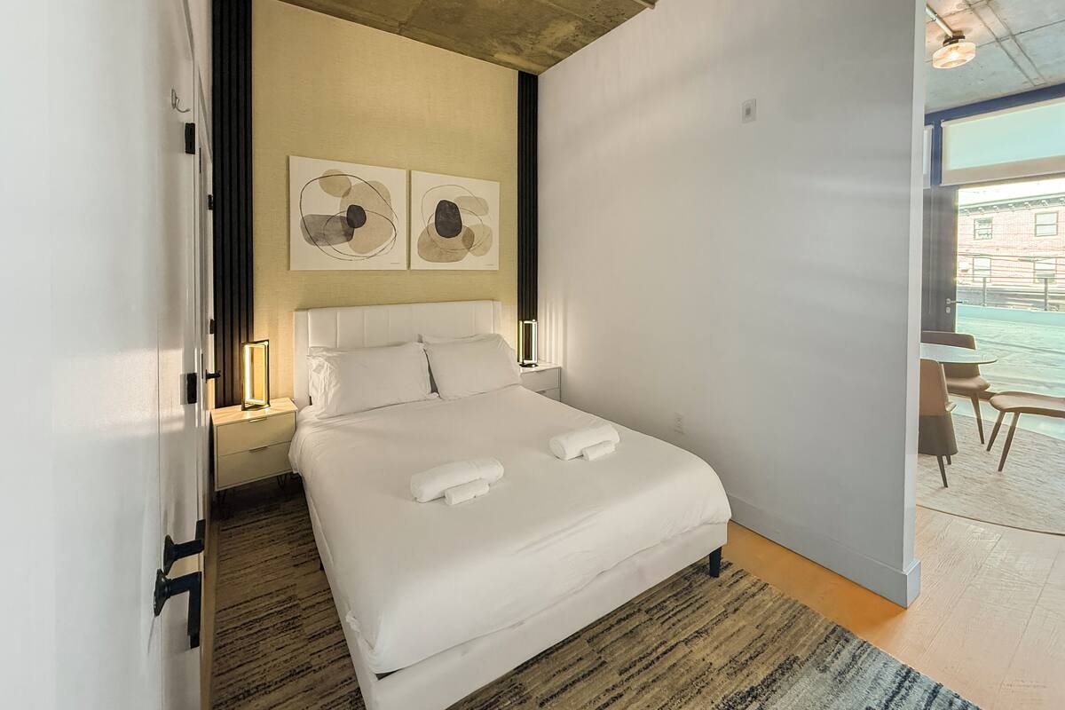 A modern hotel room with a large bed, artwork on the wall, and a view of the outside.