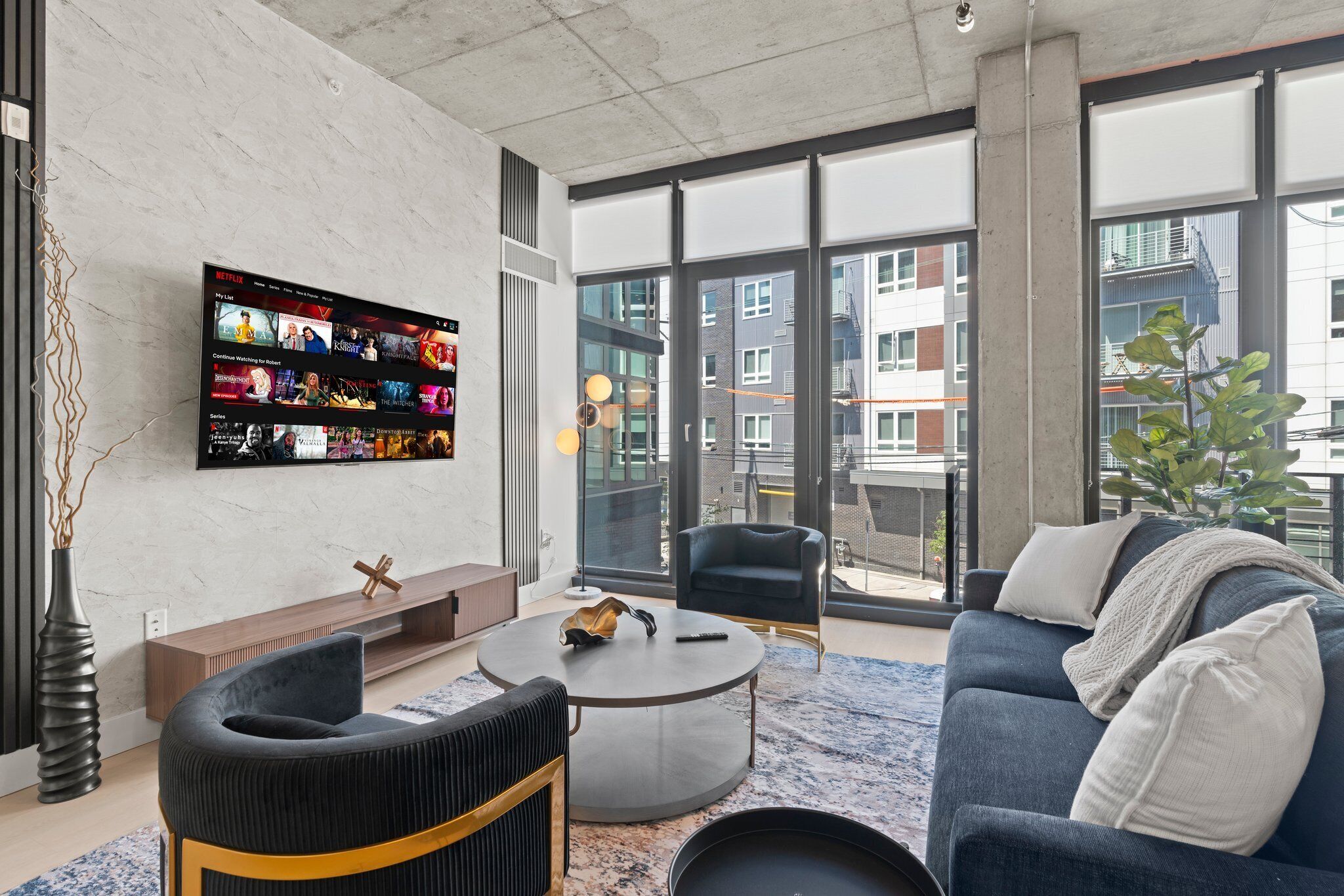 Una sala de estar moderna con un televisor grande, asientos cómodos y vistas de la ciudad a través de amplios ventanales.