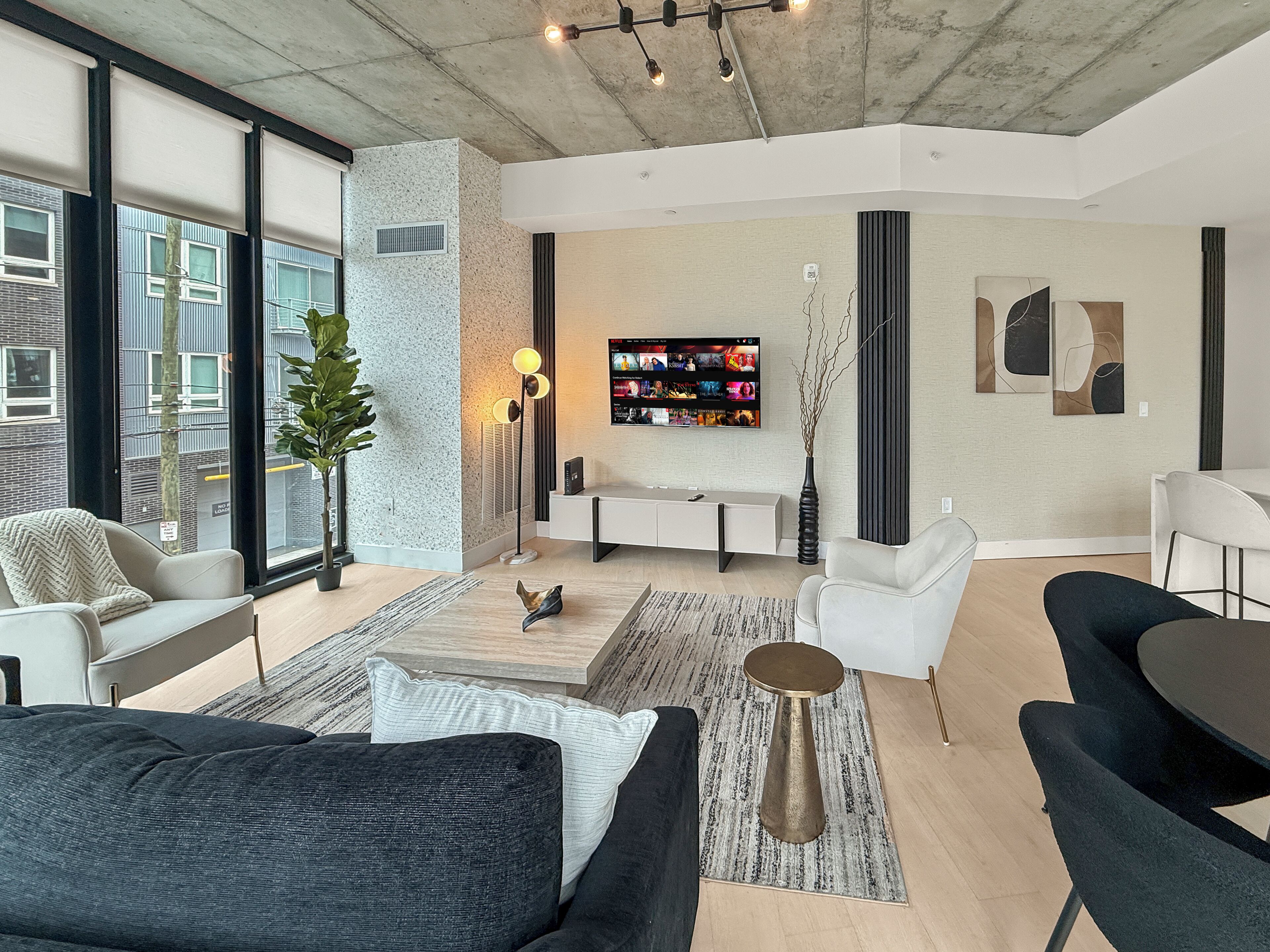 Una sala de estar moderna con un sofá, sillones, una mesa de centro, un televisor y una planta.