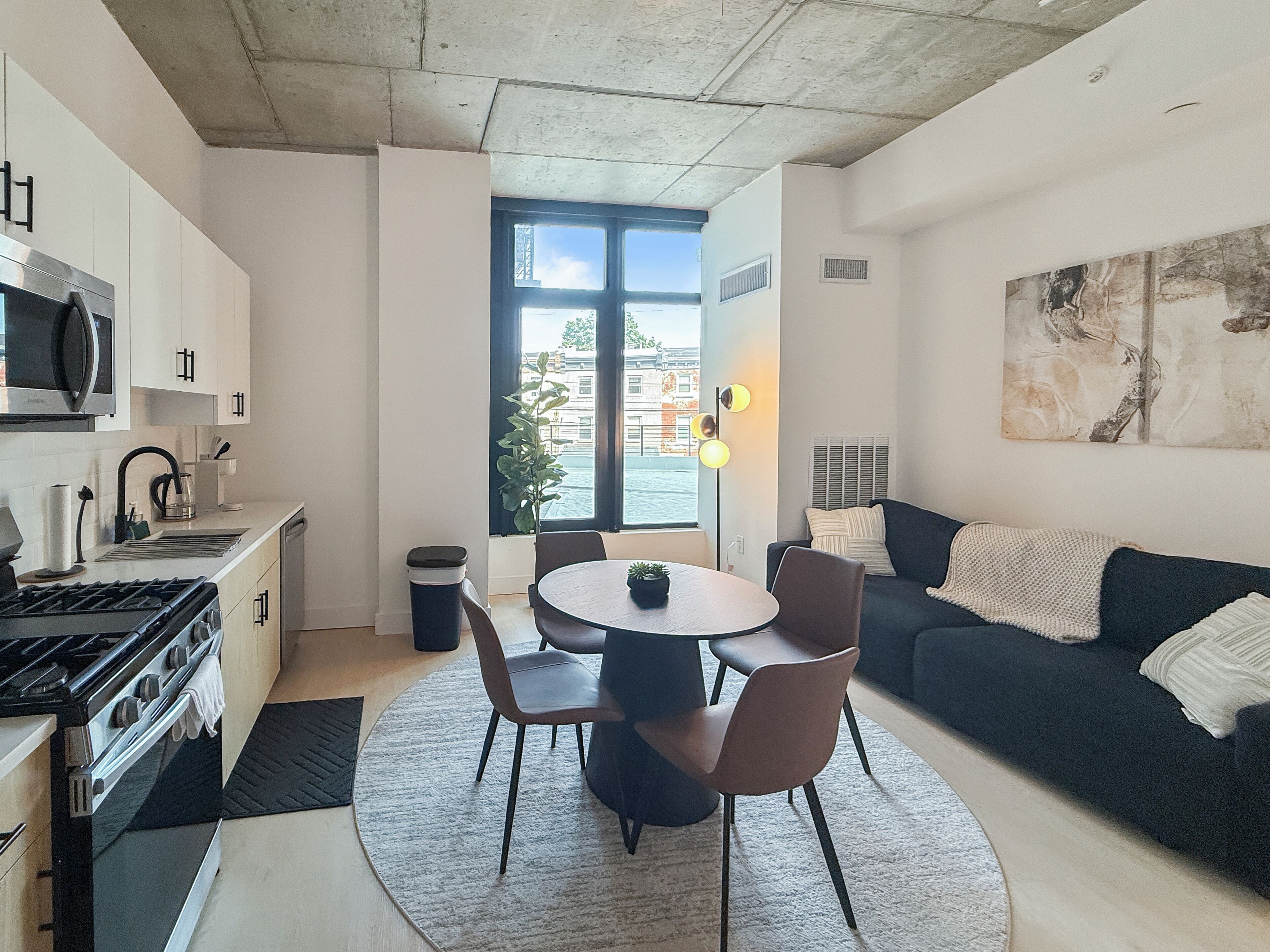 Eine moderne Küche mit Herd, Mikrowelle und Schränken, ein Essbereich mit Tisch und Stühlen sowie eine Wohnbereich mit Sofa und einem Gemälde.