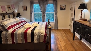 Un dormitorio con cama, cortinas en la ventana, una lámpara y un aparador.