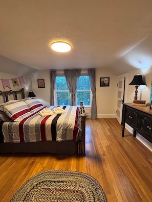 Un dormitorio con cama, cortinas en la ventana, una lámpara y un aparador.