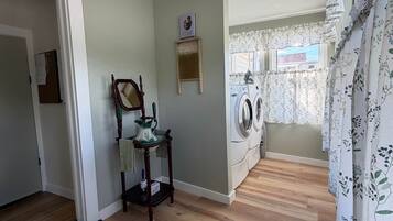 A laundry room with a washing machine, a wooden table with a pitcher, and a mirror.