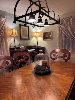Un comedor con una mesa de madera, sillas, una araña, lámparas y una jaula decorativa.