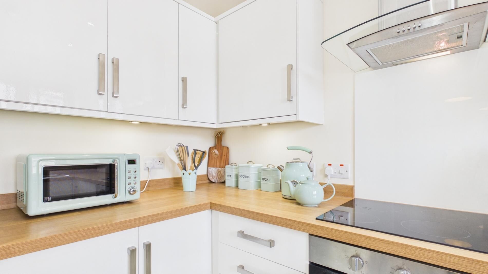 Een moderne keuken met witte kastjes, een magnetron, een waterkoker en opbergboxen.