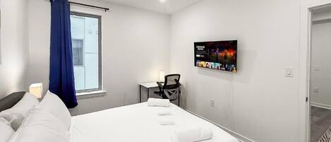 Habitación de hotel con cama, escritorio, silla, televisor en la pared y ventana con cortinas azules.