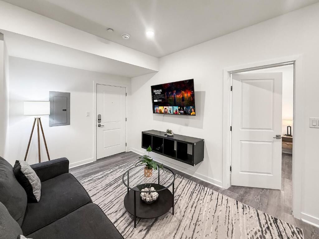 A modern living room with a sofa, a coffee table, a TV mounted on the wall, and a door leading to another room.