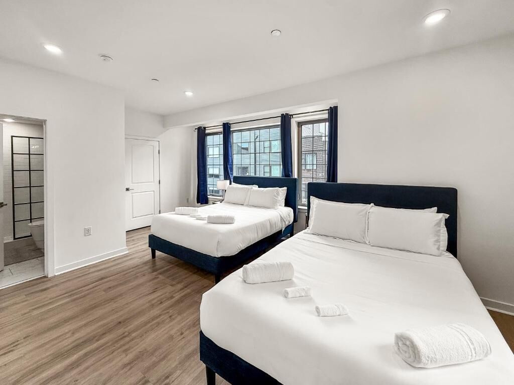 Moderni hotellihuone, jossa on kaksi sänkyä, suuri ikkuna ja puulattia.