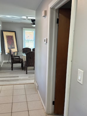 A room with a dining table and chairs, a framed picture on the wall, a thermostat, and a door leading to another room.