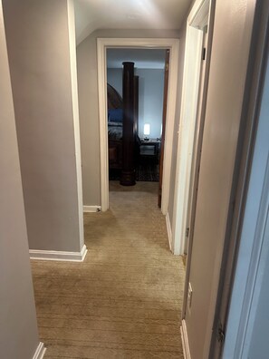 Ein Teppich ausgelegter Flur, der zu einem Schlafzimmer mit Bett, Schreibtisch und Stuhl führt.
