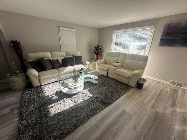 A living room with a sectional sofa, a glass coffee table, and a large window.