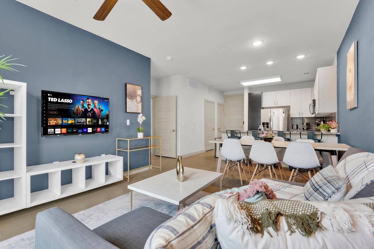 A modern living room with a flat-screen TV, a dining area, and a kitchen.
