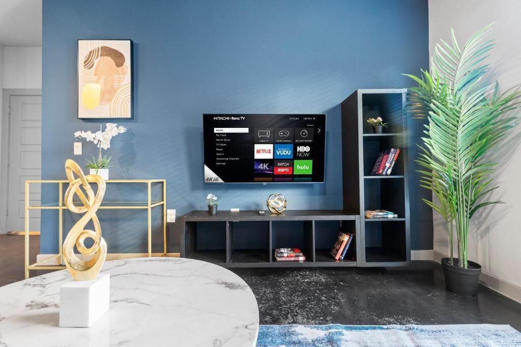 A living room with a TV, a marble table, a gold sculpture, a bookshelf, and a potted plant.