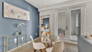 A modern living room with a dining area, a large painting, and a view through a sliding door. - Apartmint at Bell Katy Trail Dallas (Dallas)