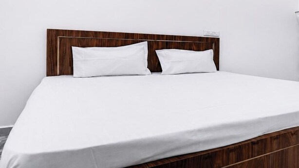Una cama con cabecera de madera, ropa de cama blanca y una pared blanca lisa.
