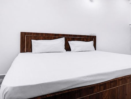 A bed with a wooden headboard, white bedding, and a plain white wall.