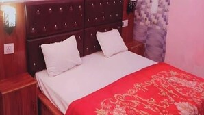 Un dormitorio con cabecera de madera, dos almohadas blancas, una colcha roja y una mesita de noche.