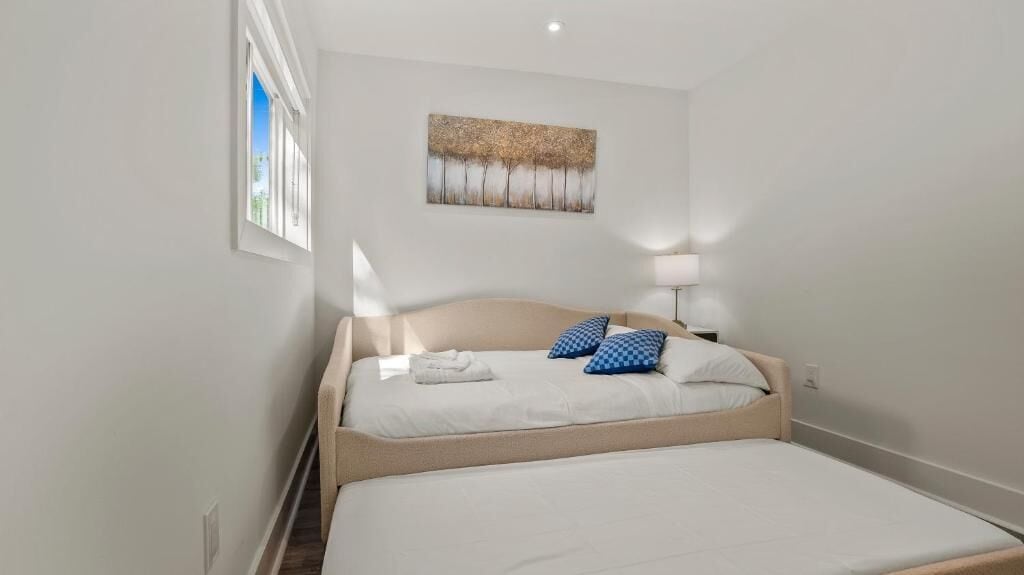 A bedroom with a bed, a painting on the wall, and a window.