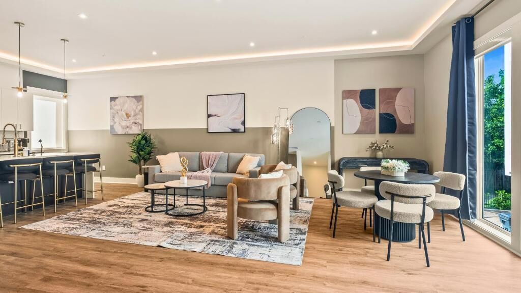 A modern living room with a sofa, coffee table, and chairs, a dining area with a table and chairs, and a kitchen area with a bar counter.