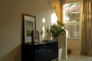 A room with a dark-colored console table, a framed picture, a potted plant, and a window with blinds. - Spacious 3-bedroom townhome in Kissimmee (Kissimmee)
