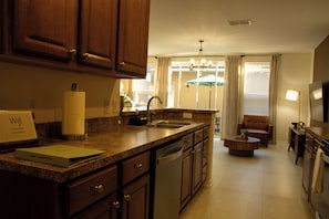 A kitchen with granite countertops, wooden cabinets, a dishwasher, and a dining area with a round table and a brown leather chair. - Spacious 3-bedroom townhome in Kissimmee (Kissimmee)