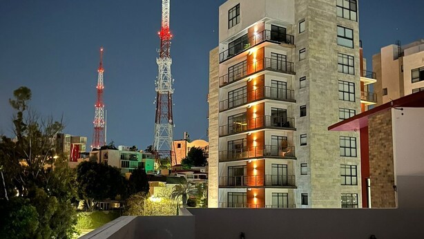 A multi-story building with balconies, a rooftop terrace, and two illuminated communication towers in the background. - La Paz Department (Heroica Puebla de Zaragoza)
