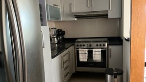 A compact kitchen with a refrigerator, stove, microwave, and a trash bin. - La Paz Department (Heroica Puebla de Zaragoza)