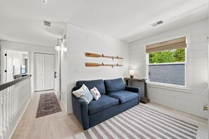 A modern living room with a blue sofa, a wooden coffee table, and a window with a view of greenery.