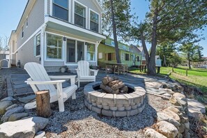 Ein Haus mit einer Terrassenanlage, ausgestattet mit Adirondack-Stühlen, einer Feuerstelle und einem Steinkamin.