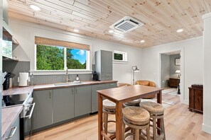 A modern kitchen with grey cabinets, a wooden dining table, and a window with a view of greenery. - Crystal Lake East End Retreat with Dock, Hot Tub & Sunset Views (Beulah)
