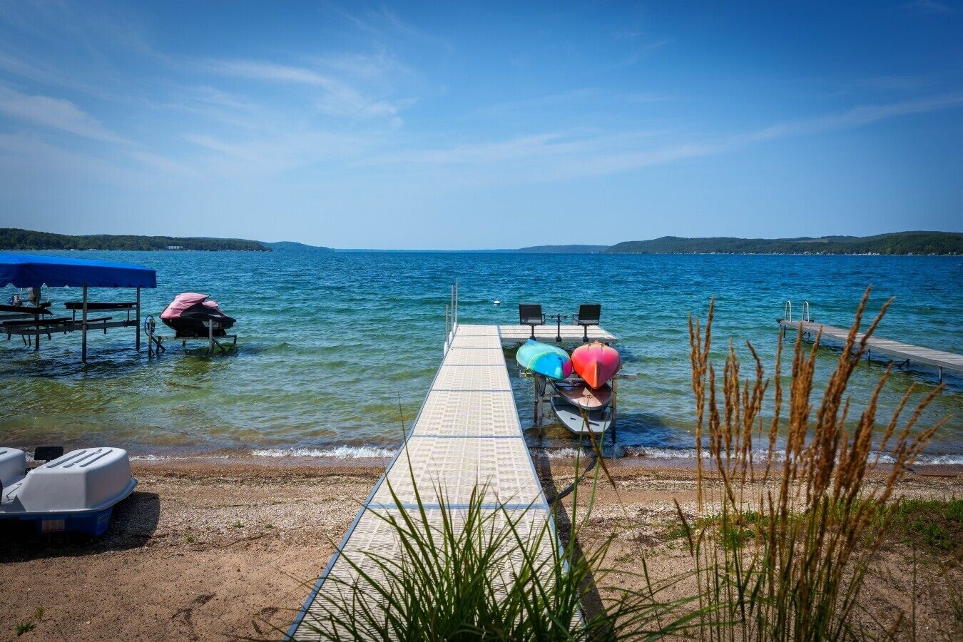 A pier leading to a calm lake with boats and a covered area on the left.