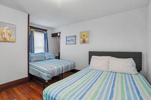 Un dormitorio con dos camas, suelo de madera y ventana con cortinas.