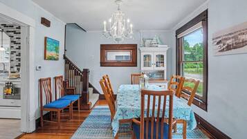 Un coin repas agrémenté d’un lustre, de chaises en bois, d’une table recouverte d’une nappe à motifs et offrant une vue sur l’extérieur grâce à une grande fenêtre.