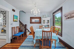 Un comedor con candelabro, sillas de madera, una mesa con mantel estampado y vistas al exterior a través de un ventanal amplio.