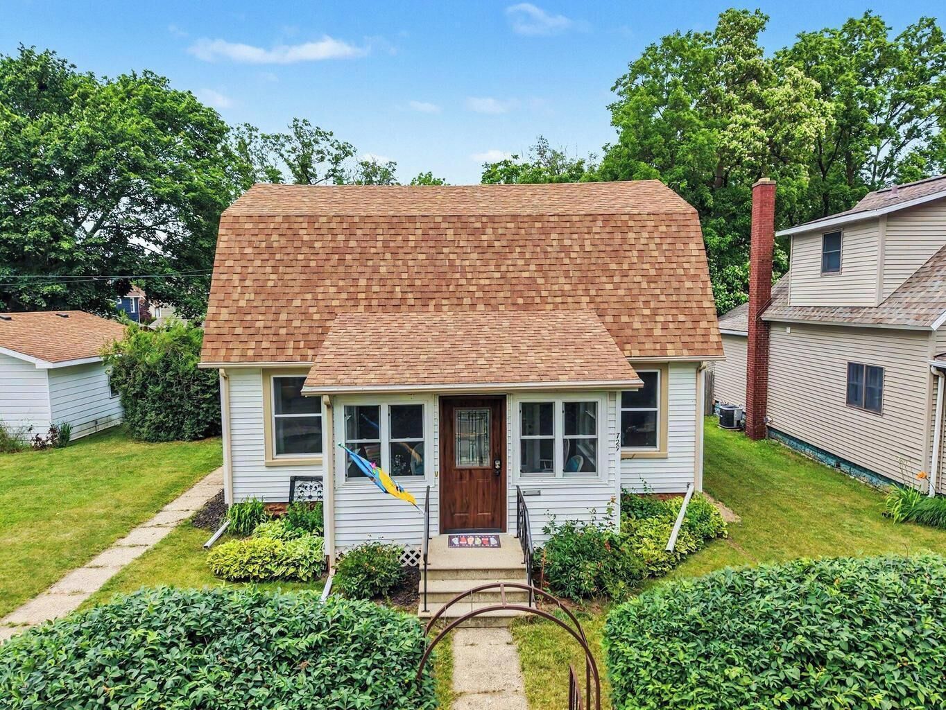 Une maison de plain-pied avec un toit en briques, un porche à l’avant et un petit jardin devant la maison.