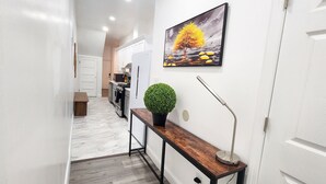Ein Flur mit einer hölzernen Sitzbank, einem Blumentopf, einer Stehlampe und einem Bild an der Wand.